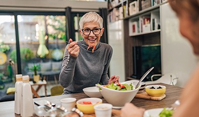Woman smiling while eating lunch with friend in kitchen