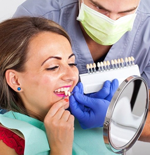woman in the dental chair holding veneers up to her smile