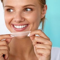 woman smiling while holding teeth whitening strip 