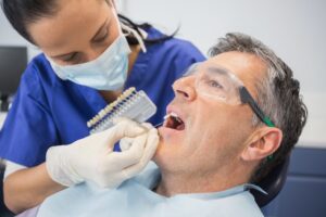 Dentist placing veneer on older man's teeth.